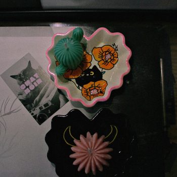 Two heart shaped trays one white with a floral motif and a black cat, one black with a cow skull painted on