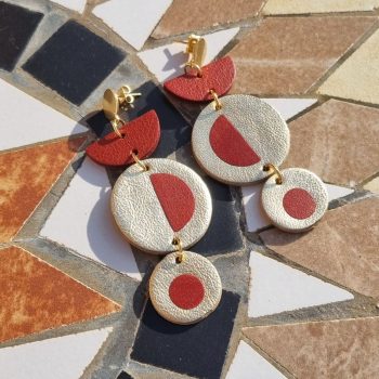 Gold and brick red inlayed dangly earrings on a tiled table.